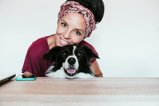 Smiling woman embracing Border Collie against white wall at home