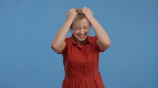 A grown woman who desperately pulls her hair out as if something extremely bad has happened. Slow motion.Studio shot isolated on blue background.Portrait of a woman feeling bad, pulling her crazy hair