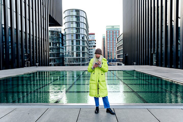 Young woman using smart phone while standing against skyscrapers in city