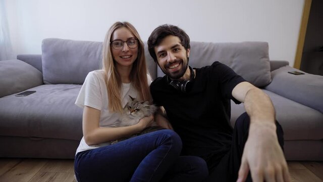 Beautiful young couple with their cat on their living room couch talking to the camera