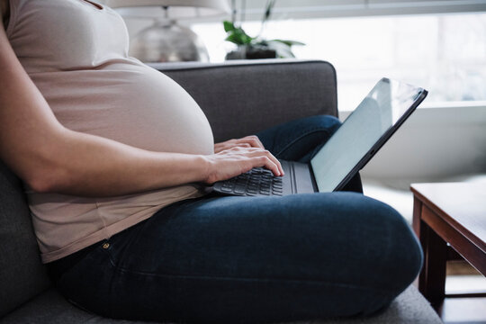 Pregnant woman using laptop while sitting on sofa at home