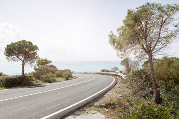 A beautiful winBeautiful winding road against the background of the sea and sky. Sunny day, trees. Cyprus.ding road in the mountains against the background of the sea and sky. . High quality photo