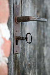Old wood door with key, door handle, and detail of rust and patina. 