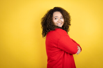 Young african american woman wearing red sweater over yellow background looking to the side with arms crossed convinced and confident