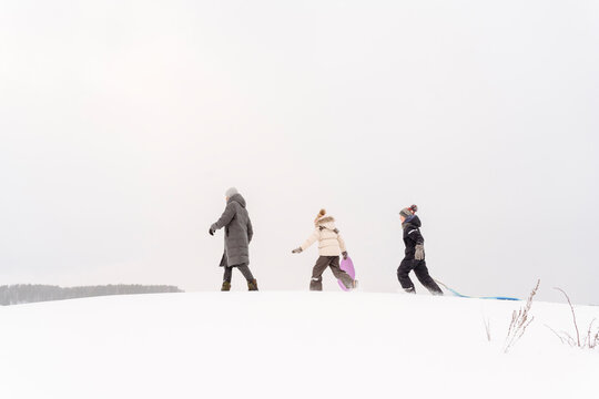 Father and children walking with sleds on snow covered land against sky