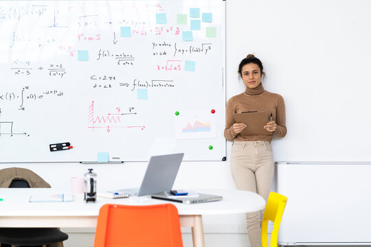 Female student with clipboard standing by whiteboard at home