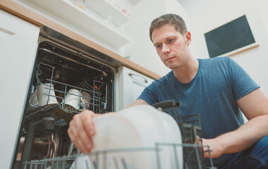 Man puts glass to the dishwasher in the kitchen.