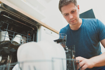 Man puts glass to the dishwasher in the kitchen.