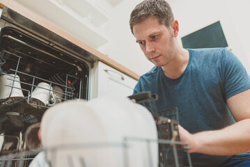 Man puts glass to the dishwasher in the kitchen.