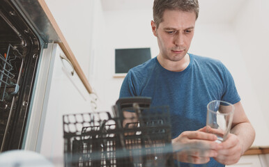 Man puts glass to the dishwasher in the kitchen.
