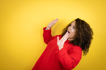 Young african american woman wearing red sweater over yellow background scared with her arms up like something falling from above