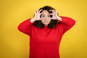 Young african american woman wearing red sweater over yellow background Trying to open eyes with fingers, sleepy and tired for morning fatigue