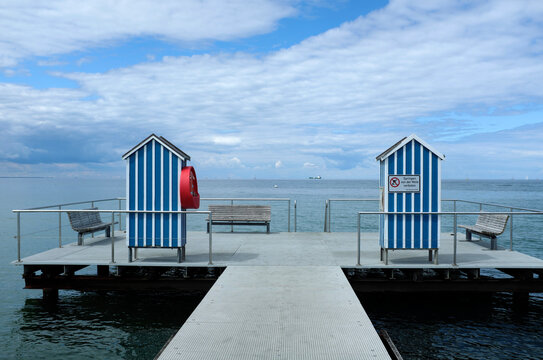 Germany, Schleswig Holstein, Stein, Jetty with blue and white beach cabins on Baltic Sea under cloudy sky