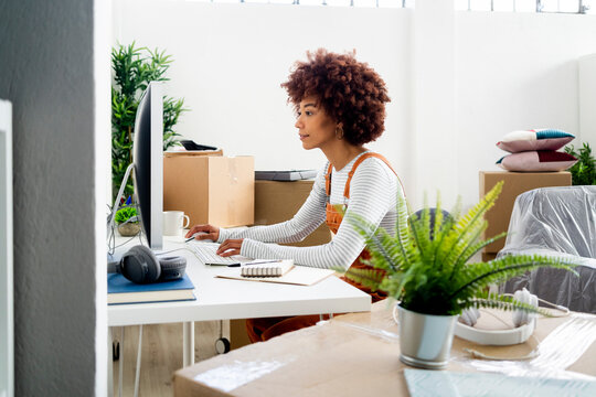 Afro woman using computer while surrounded by cardboard boxes in new home