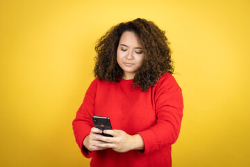 Young african american woman wearing red sweater over yellow background texting with her phone