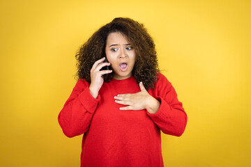 Young african american woman wearing red sweater over yellow background talking on the phone with a worried expression