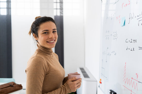 Smiling woman holding coffee cup while standing in front of whiteboard at home