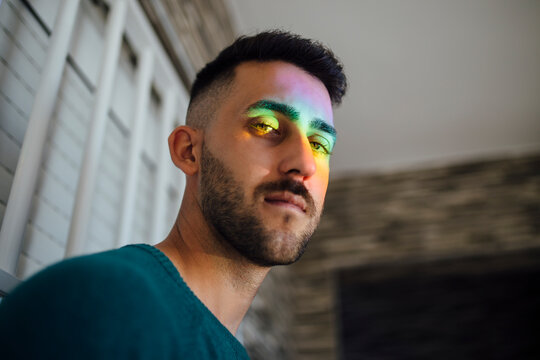Rainbow light hitting face of young man looking down at camera