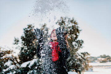 Playful woman throwing snow while enjoying winter at countryside against clear sky