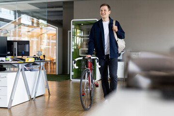 Smiling businessman with bag and bicycle walking while leaving after work from office