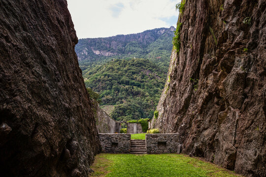 Grass lane amidst soapstone cliffs at quarry in Parco Archeologico Botanico del Paradiso, Valchiavenna, Chiavenna, Province of Sondrio, Lombardy, Italy
