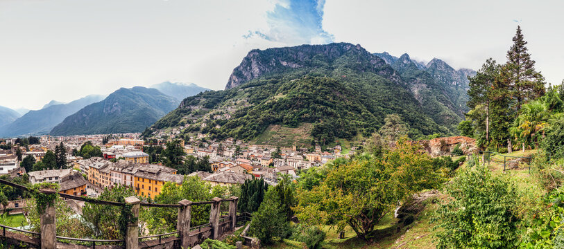 Townscape seen through Parco Archeologico Botanico del Paradiso against mountains in Valchiavenna, Chiavenna, Province of Sondrio, Lombardy, Italy