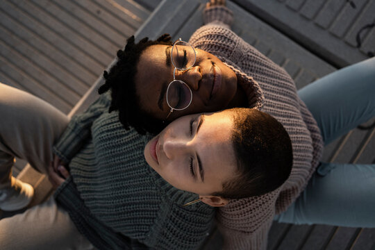 Young women leaning on each other shoulder while sitting on bench