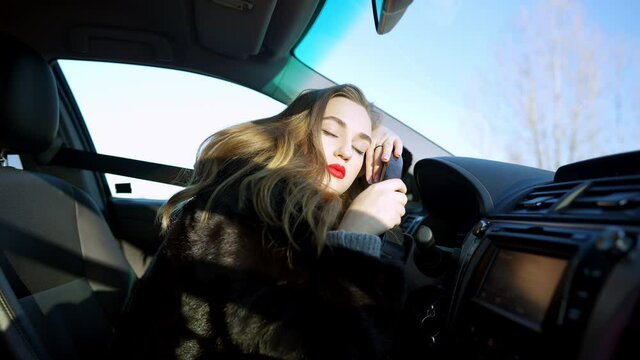 Beautiful brunette woman getting asleep on steering wheel in car. Portrait of slim young Caucasian elegant lady sleeping in automobile on sunny day. Tiredness and exhaustion.