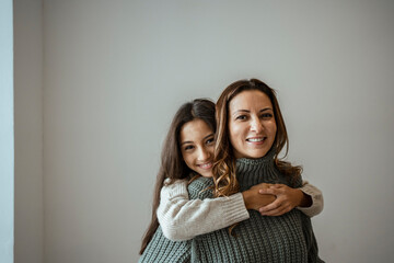 Happy daughter embracing mother while standing against white wall at home