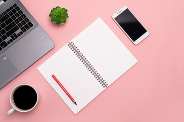 flat lay, view from the top of the office desk table. Working space notepad, laptop, phone and coffee cup on a pink background