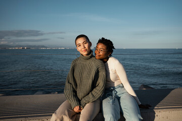 Woman leaning on friend shoulder while sitting on bench against sky