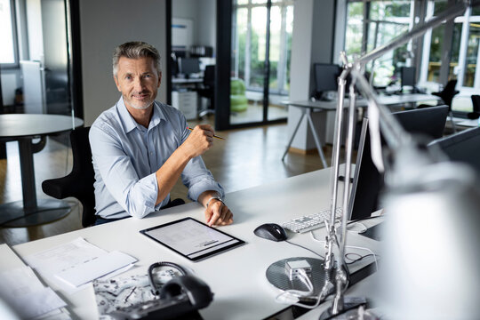 Mature entrepreneur with digital tablet smiling while sitting at office