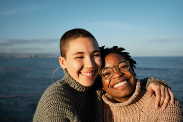 Female friends smiling while sitting against sea