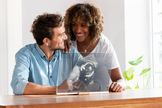 Couple smiling while checking ultrasound image over transparent screen at home