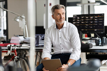 Mature businessman with digital tablet looking away while sitting at office