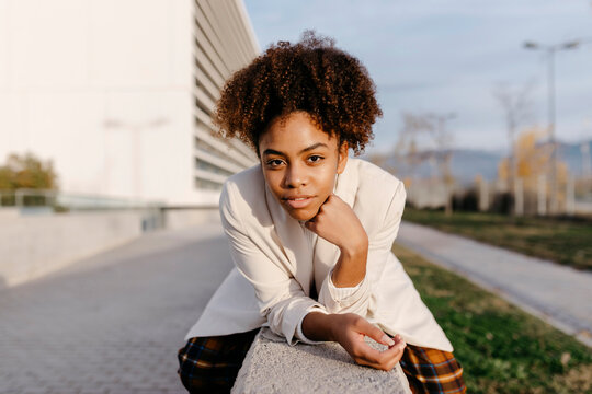 Confident young woman with afro hair sitting on retaining wall in city