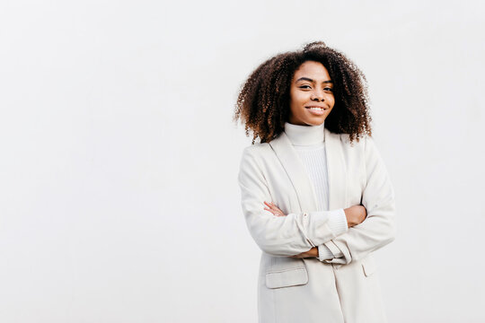 Smiling afro young woman with arms crossed standing against white wall