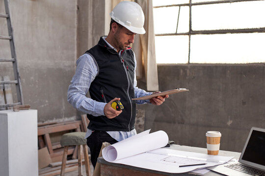 Male building contractor analyzing plan while standing at table in building