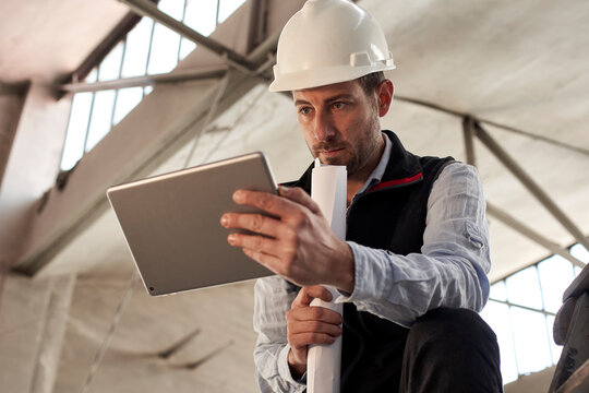 Serious male engineer using digital tablet while standing in building at site