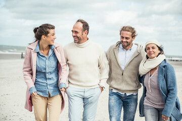 Group of adult friends walking side by side along sandy beach