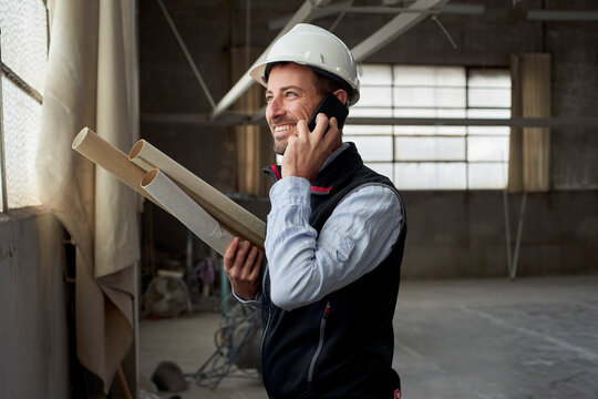 Smiling Male Building Contractor Talking Over Smart Phone Inside Construction Site