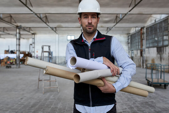 Confident male architect holding cardboards while standing in building