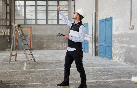 Male architect with digital tablet pointing while looking up in constructing building