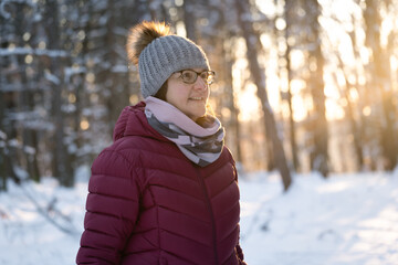 Portrait of middle aged caucasian woman in winter forest. Mature woman looking away from camera and enjoying beautiful winter, snow and sun