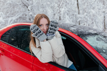Happy woman looks out the car window, covering her face with her hands. Winter forest.