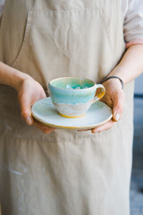 person in the apron holding handmade clay and turquoise cup of tea