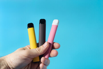 Disposable electronic cigarettes in hand closeup on a blue background. The concept of modern...