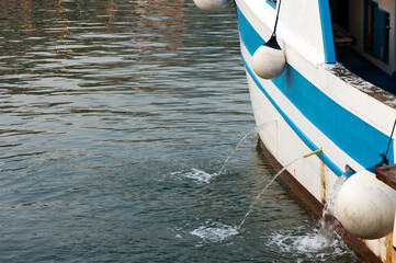 The portside of a fishing boat berthed in the harbor. Water drainage 