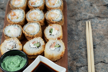 Fried hot sushi rolls with cream cheese, wasabi and soy sauce on a wooden board
