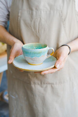 person in the apron holding handmade clay and turquoise cup of tea